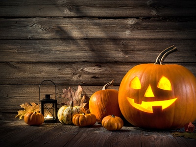 A jack-o-lantern, pumpkins, and a candle light sitting on a porch